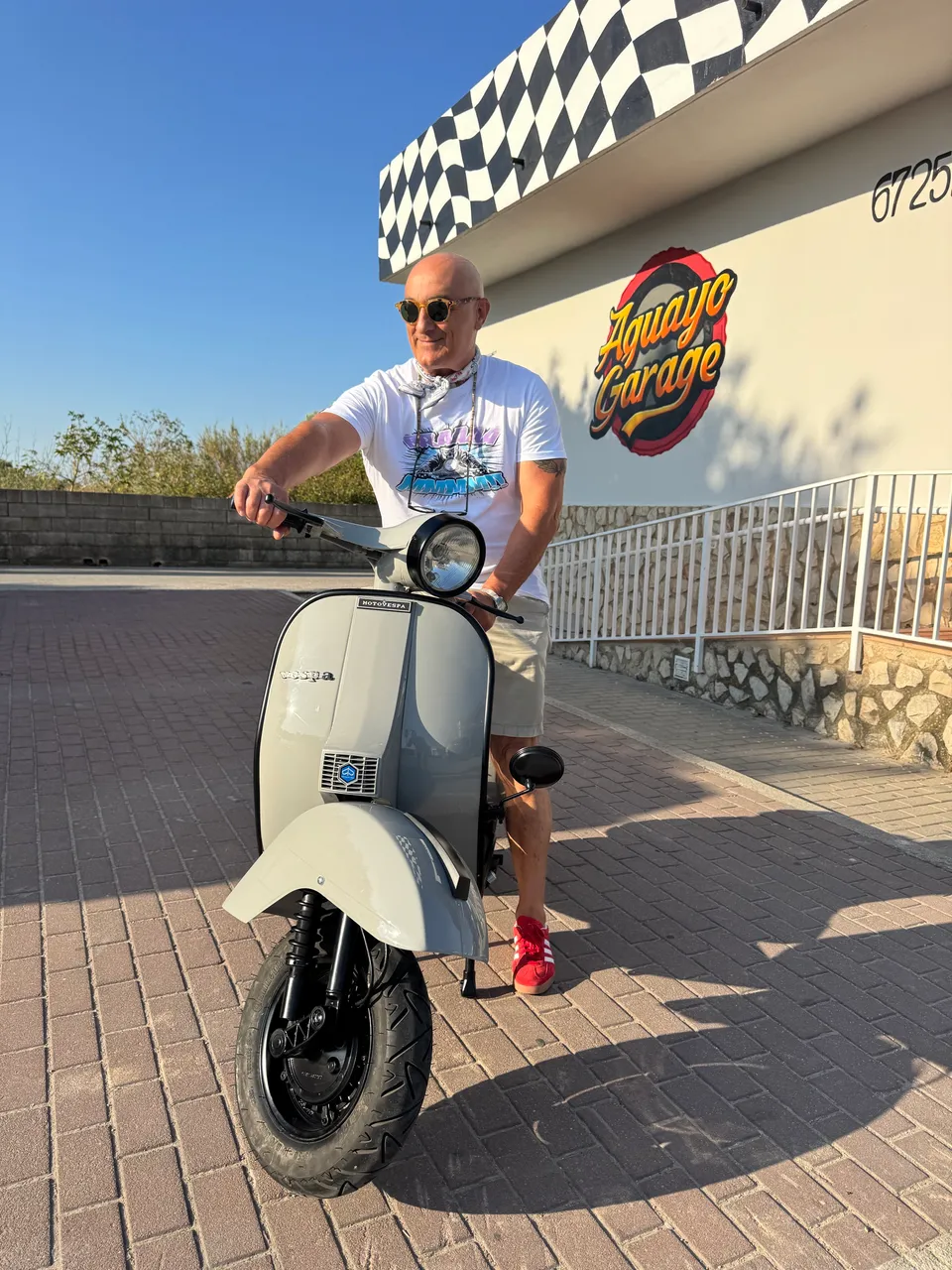 Una persona sentada en una Vespa crema recién restaurada, delante de la fachada del taller.