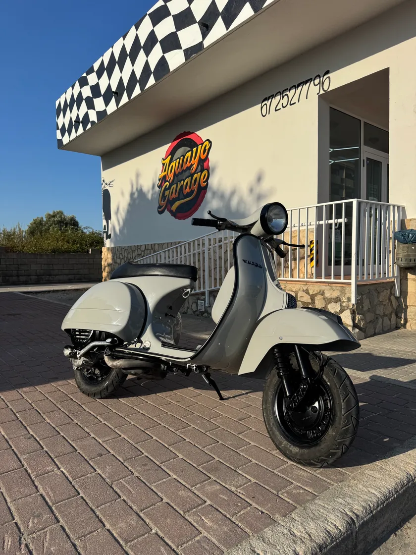 La misma moto ya restaurada, de perfil en la puerta del taller, con la pintura crema uniforme.